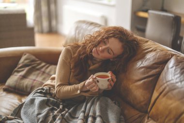 Üzgün bir genç kadın kanepede uzanıyor ve telefonla konuşuyor.