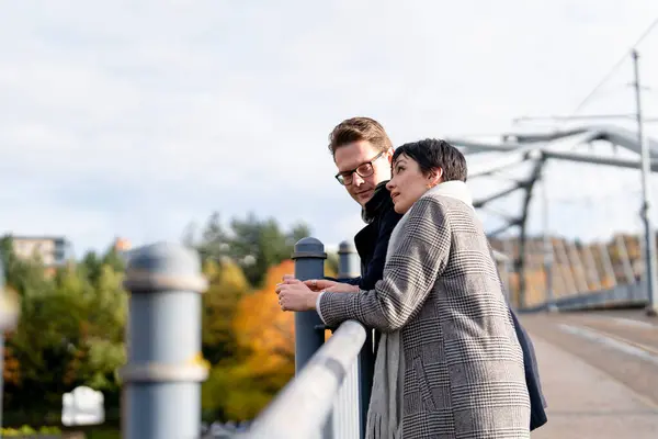 Handsome man and beautiful woman falling in love, hugging each other, looking from a bridge  as they walk around a city, having a fun time, lifestyle photo