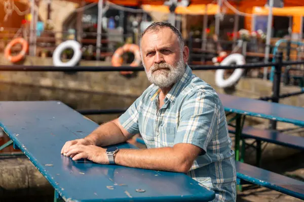 stock image a mature bearded man sitting  on a bench, walking at a quay, enjoying warm days of the spring, summer