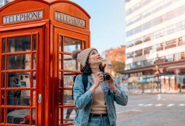 Outdoor portrait of woman using camera   against red phonebox in English city