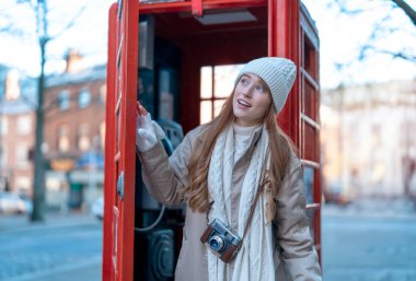 Outdoor portrait of woman using camera   against red phonebox in English city