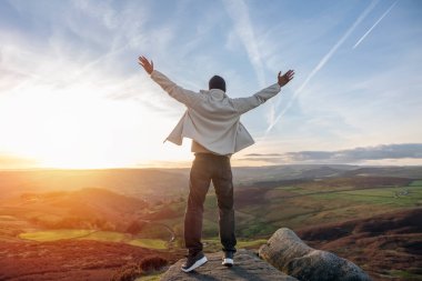 Sırt çantasıyla gezen ve İngiltere 'de gün batımında dağların tadını çıkaran yakışıklı turist. Sırt çantasıyla dağlara bir gezi. Yürüyüşün ve yeni yerler keşfetmenin tadını çıkarın.