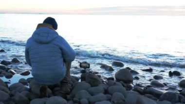 Deniz kenarında tek başına dinlenen ve soğuk kış günü gün batımında telefonda zaman ayarlı konuşan bir adam. Seyahat yaşam tarzı konsepti