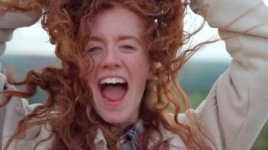 Kızıl saçlının altın saatindeki neşeli anı. Parlak kırmızı bukleleri olan mutlu genç bir kadın. 