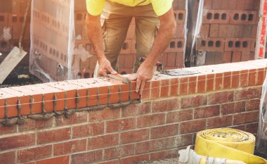 Industrial bricklayer laying bricks on cement mix on construction site