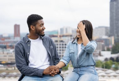 Yakışıklı bir adam ve güzel bir kadın sırtüstü oturmuş modern bir şehrin önünde geleceği hayal ediyorlar.