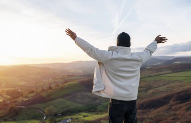 Sırt çantasıyla gezen ve İngiltere 'de gün batımında dağların tadını çıkaran yakışıklı turist. Sırt çantasıyla dağlara bir gezi. Yürüyüşün ve yeni yerler keşfetmenin tadını çıkarın.