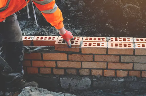 İnşaat alanındaki çimento karışımına tuğla döşeyen endüstriyel tuğla ustası. Konut krizine karşı daha ekonomik konutlar inşa ederek mücadele etmek