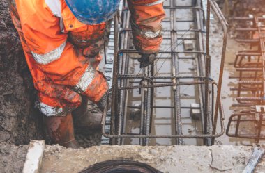 Bir işçi demir çubukları birbirine bağlamak için çelik teller kullanır. Güçlendirilmiş beton yapılar. Beton kiriş için çelik bir kafes yapıyorlar.