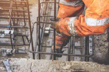 Bir işçi demir çubukları birbirine bağlamak için çelik teller kullanır. Güçlendirilmiş beton yapılar. Beton kiriş için çelik bir kafes yapıyorlar.