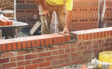 Industrial bricklayer laying bricks on cement mix on construction site