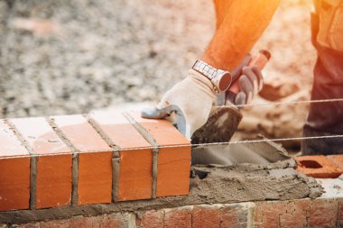 Industrial bricklayer laying bricks on cement mix on construction site close-up