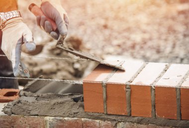 Industrial bricklayer laying bricks on cement mix on construction site close-up