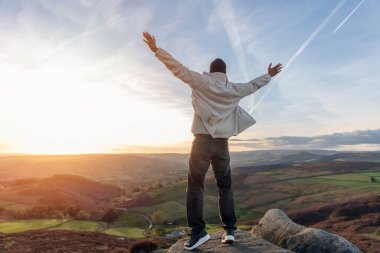 Sırt çantasıyla gezen ve İngiltere 'de gün batımında dağların tadını çıkaran yakışıklı turist. Sırt çantasıyla dağlara bir gezi. Yürüyüşün ve yeni yerler keşfetmenin tadını çıkarın.