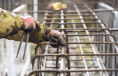 Bir işçi demir çubukları birbirine bağlamak için çelik teller kullanır. Güçlendirilmiş beton yapılar. Beton kiriş için çelik bir kafes yapıyorlar.