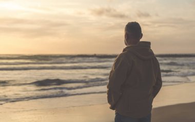 Sırt çantalı sakallı adam gün batımında sıcak güneşli bir günde deniz kenarında tek başına dinleniyor. Tonlanmış görüntü. Seyahat yaşam tarzı konsepti
