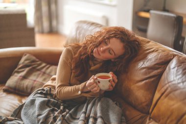 Üzgün bir genç kadın kanepede uzanıyor ve telefonla konuşuyor.
