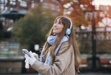 Genç bir kadın eğleniyor, telefon kullanıyor, müzik dinliyor ve şehirde dans ediyor. İnsanlar, iletişim, alışveriş ve yaşam tarzı kavramı