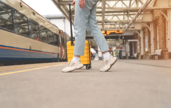 stock image Traveler with a yellow suitcase waiting for a train at the train station on the platform. Travel concept.