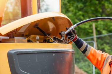 Builder in safety gloves filling excavator with diesel fuel on building site clipart