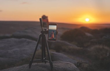 Peak District 'te gün doğumunda ya da günbatımında fotoğraf ya da görüntü çeken bir tripodun üzerinde telefon.