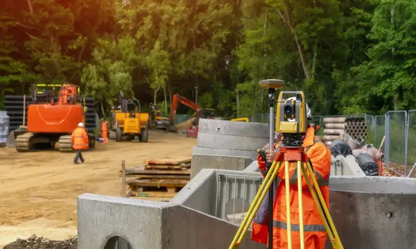 stock image Surveyor site engineer with total positioning station on the construction site of the new road construction with construction machinery and materials  in the background