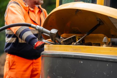 Builder in safety gloves filling excavator with diesel fuel on building site clipart