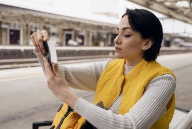 Pasaportu ve biletleri olan genç bir kadın tren istasyonunda tren bekliyor. Seyahat kavramının tadını çıkarıyor.