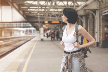 Tren istasyonunda sırt çantalı mutlu bir kadın ve tren geliyor. Seyahat kavramının tadını çıkar