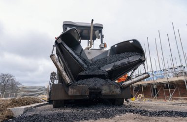 Sıcak asfalt kaldırım taşı yeni yerleşim alanı üzerine yeni yol yüzeyi döşeyen ve yanında turuncu hi-viz 'deki yol işçisi operatörü