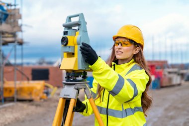 Bir inşaat şantiyesinde Theodolite toplam istasyon EDM ekipmanıyla çalışan kadın inşaat mühendisi araştırmacısı.
