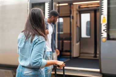 Bavulları ve sırt çantaları ile mutlu bir çift tren yolu platformu boyunca yürüyorlar ve tatile çıkmaya hazırlar. Erkek ve kadın el ele tutuşuyor, geriye bakıyor ve gülümsüyor. Tren konseptiyle seyahat