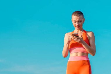 Parkta egzersiz yaptıktan sonra telefonu kullanan kısa saçlı olgun bir kadın. Yaşam tarzı spor yaşam konsepti