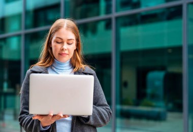 Portrait of a beautiful serious lady reading e-mails on the laptop while sitting on the steps outside of the business centre clipart