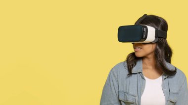 Modern VR kulaklıklı kadın sarı arka planda sanal gerçeklik evrenini keşfediyor.