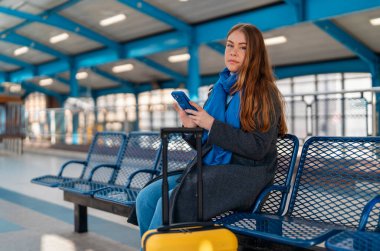 Tren istasyonunda, havaalanında, otobüs durağında akıllı telefon tutan heyecanlı bir kadın. Güvenli seyahat kavramı