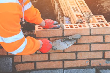 Close up of industrial bricklayer laying bricks on cement mix on construction site