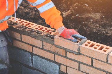 Industrial bricklayer laying bricks on cement mix on construction site. Fighting housing crisis by building more affordable houses concept