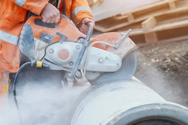 İnşaat işçisi kesme testeresi kullanarak beton boruları kesiyor. Elmas bir bıçakla beton kesmek silis tozu bulutu yaratır.