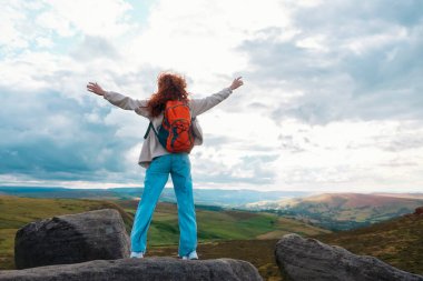 Turuncu sırt çantalı kızıl saçlı harika bir kadın ellerini kaldırıyor, gideceği yere ulaşıyor ve bulutlu bir günde dağların zirvesinde manzaranın tadını çıkarıyor. Yeni yerler keşfetmekten zevk alın.