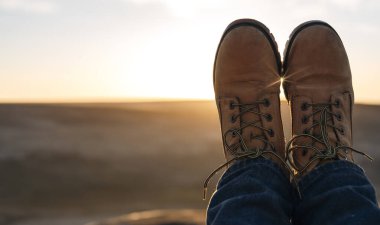 Kadının ayakları hedefe ulaşıyor ve gün doğumunda tepenin ya da dağın tepesinde oturuyor. İngiliz soğuk kışı. Yerel turizm konsepti.