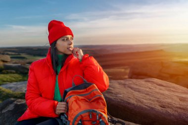 Sırt çantasıyla gezen ve İngiltere 'de gün batımında dağların tadını çıkaran gülümseyen güzel kadın turistin portresi. Sırt çantasıyla dağlara bir gezi.