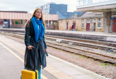 Sarı valizli bir kadın tren istasyonunda tren bekliyor. Seyahat kavramı.