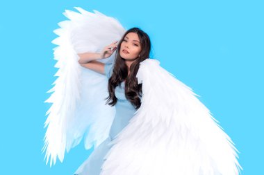 Stüdyoda mavi arka planda oturan büyük melek kanatlarıyla mavi elbiseli güzel genç bir manken..