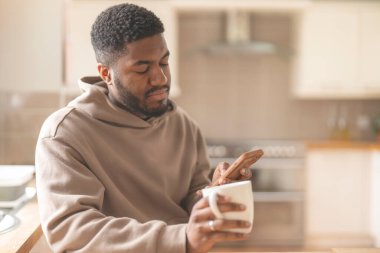 Kahverengi kapüşonlu mutlu adam telefon kullanıyor, çalışıyor, öğreniyor, alışveriş yapıyor, internette çalışıyor, evde bir kanepede otururken konuşuyor.