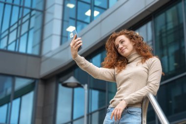 Memnun genç ve mutsuz bir kadın cep telefonuyla konuşuyor ve kullanıyor, modern bir şehirde cep telefonu kullanıyor. Yaşam tarzı fotoğrafları