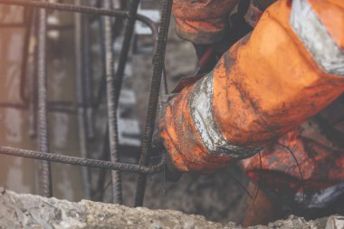 Bir işçi demir çubukları birbirine bağlamak için çelik teller kullanır. Güçlendirilmiş beton yapılar. Beton kiriş için çelik bir kafes yapıyorlar.