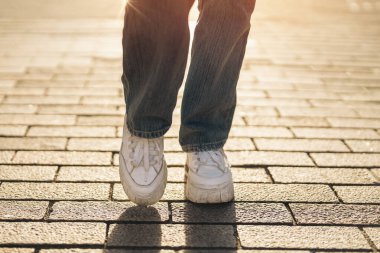 Genç kız öğrencinin bacakları eğleniyor ve gün batımında şehirde asfalt bir sokakta yürüyor.