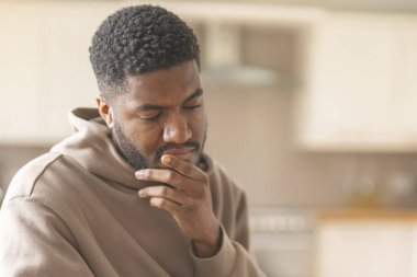 Kahverengi kapüşonlu düşünceli bir adam telefon kullanıyor, çalışıyor, öğreniyor, alışveriş yapıyor, internette çalışıyor, evde bir kanepede otururken konuşuyor.