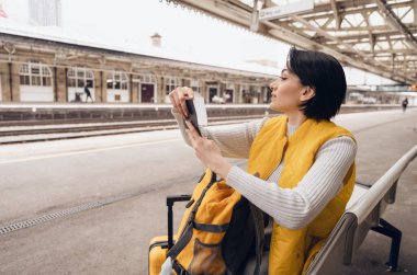Pasaportu ve biletleri olan genç bir kadın tren istasyonunda tren bekliyor. Seyahat kavramının tadını çıkarıyor.